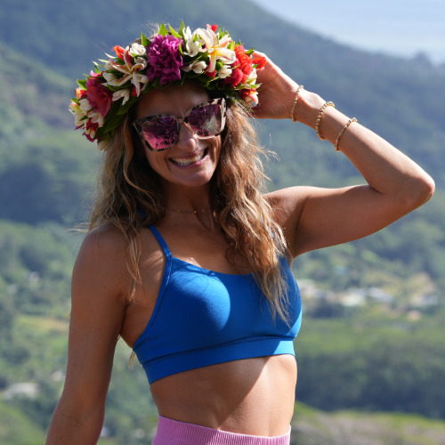 Amy Quinn Woman with a flower crown in a blue top and sunglasses, smiling.