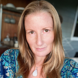 Woman wearing a blue top and a necklace with a white pendant looking into the camera.