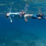 Two people snorkelling in blue waters, not too deep.