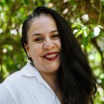 woman with long dark wavy hair smiling into the camera.