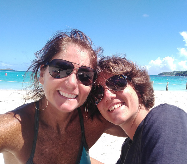 A woman and a young man taking a selfie on the beach with turquoise ocean in the background. They smile happily into the camera.